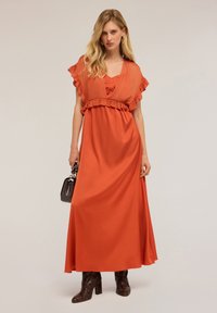 Vestido maxi de tejido color óxido con mangas con volantes y detalle en la cintura. Combinado con un bolso estructurado negro y tacones de bloque con patrón de piel de serpiente.