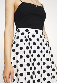 Débardeur noir à côtes associé à une jupe blanche avec de grands pois noirs, présentant un design plissé et une texture douce.