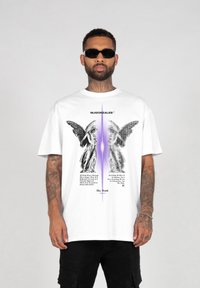 White oversized t-shirt featuring printed angel graphics and text, with a central purple gradient. Made from cotton blend, relaxed fit design.