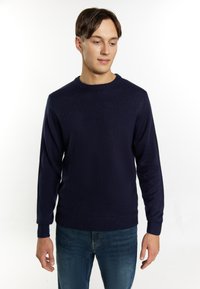 Maglione blu navy realizzato in tessuto a maglia testurizzata, con colletto a girocollo e polsini a coste. Abbinato a jeans blu di denim.