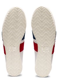 Paire de semelles blanches de chaussures avec motif de bande en chevrons, affichant le logo Onitsuka Tiger et des bandes latérales rouges et bleues.