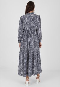 Vestido maxi en azul oscuro con un patrón floral blanco; cuenta con mangas largas abullonadas, una cintura ajustada y un dobladillo de volantes en capas.