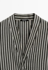Top noué à rayures noires et blanches avec un décolleté en V, texture douce, et une étiquette indiquant "Massimo Dutti, fabriqué au Portugal."