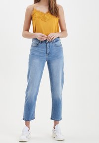 Yellow camisole with lace trim, paired with light blue high-waisted jeans, featuring a relaxed fit and ankle-length hem, worn with white sneakers.