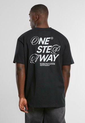 Sort bomuld t-shirt med stort hvidt tekst på ryggen, der siger "ONE STEP AWAY" med dekorative elementer. Korte ærmer, afslappet pasform.