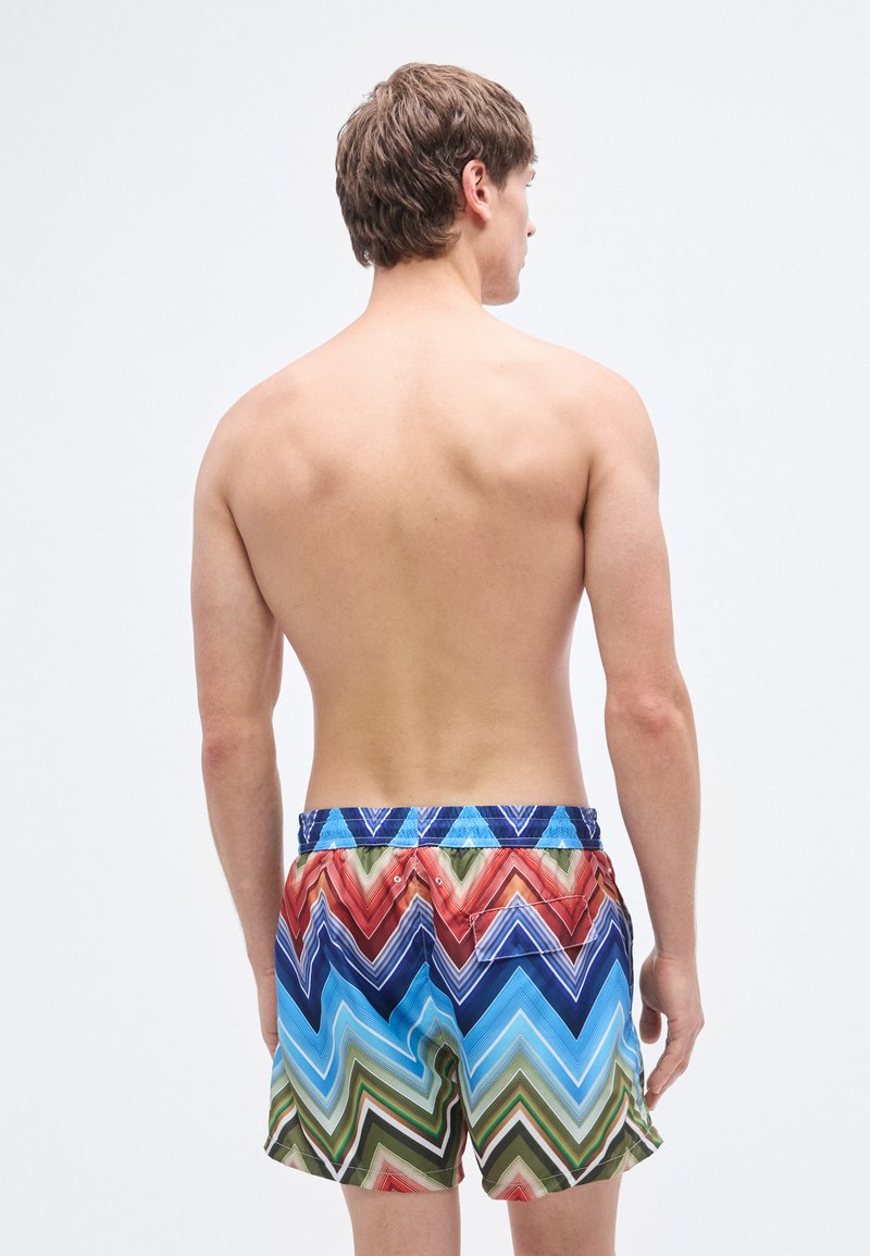 Costume da bagno colorato con motivo a zigzag in tonalità di blu, rosso, verde e arancione. Presenta una fascia elastica in vita e una tasca posteriore.