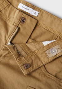 Pantalons beige en mélange de coton avec fermeture éclair, bouton de fermeture et détails cousus. L'étiquette indique "name it" avec la taille 128.