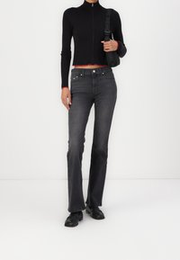 Černý žebrovaný zipový top s červeným lemem; tmavě šedé vysoké kalhoty s rozšířenými nohavicemi; doplněno černými botami; minimální doplňky.