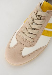Sneaker con materiali in suede beige e pelle bianca, con accenti gialli e lacci grigio chiaro. Forma arrotondata con dettagli cuciti.