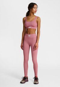 Roze geribbelde sportbeha en bijpassende hoge taille legging, gemaakt van rekbare stof. Zwart-grijze sneakers met rode accenten maken de outfit compleet.