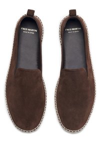 Chaussures brunes en daim à enfiler avec un bout arrondi, des coutures contrastées le long de la semelle, et une languette cousue à l'arrière.
