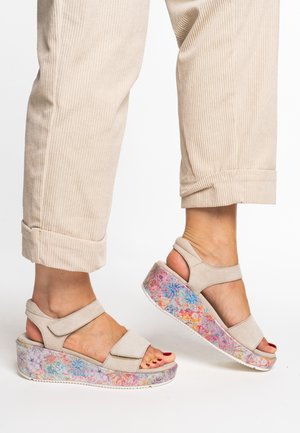 Beige wedge sandals with a floral patterned platform. Features two adjustable straps and a cushioned sole for comfort.