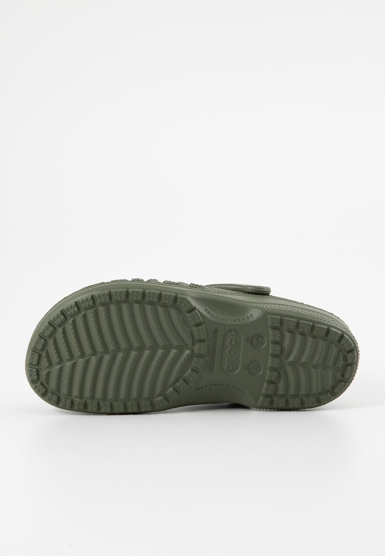 Des chaussures en caoutchouc vert, dotées d'une semelle texturée avec des motifs de crantage contrastés et le logo "CROCS" en relief au fond.