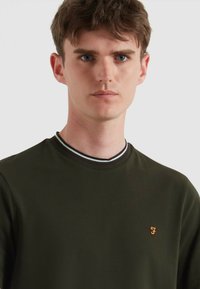 Maglietta a manica lunga verde scuro con collo a girocollo rigato, caratterizzata da un bordo multi-colore e un piccolo logo ricamato sul petto.