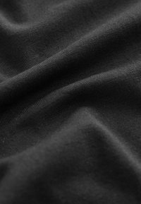 Gros plan d'un tissu noir avec une texture tricotée visible et des plis doux créant des ombres et des reflets doux.