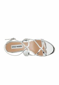 Sandal con tacco alto argento con cinturini incrociati e un accento circolare, caratterizzato da una texture lucida e un sottopiede imbottito beige.
