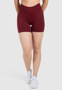 Shorts bordeaux a vita alta con un design aderente e una texture liscia, abbinati a scarpe da ginnastica bianche su uno sfondo neutro.
