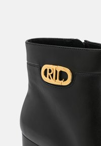 Botín de cuero negro hasta el tobillo con forma redondeada y un acento dorado del logo "RL" en el lateral. Textura suave con detalles de costura.