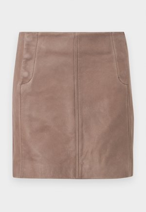 Woman wearing a brown ribbed long-sleeve polo top, beige mini skirt with pockets, and black high-heeled sandals, standing against a plain background.