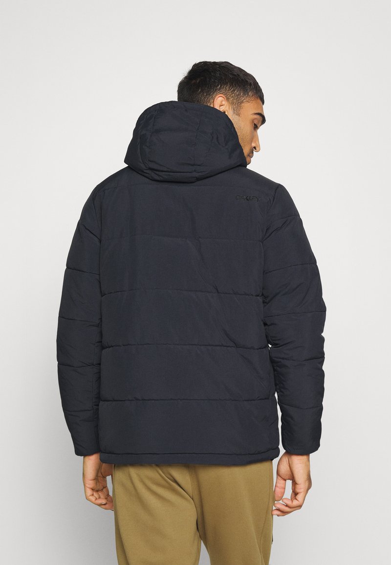 Giacca imbottita blu scuro con cappuccio, caratterizzata da cuciture orizzontali, una texture liscia e un logo sulla parte superiore della schiena.