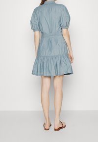 Světle modré denimové šaty s límečkem, krátkými puff rukávy, páskem v pase a volánkovým lemem. Hladká textura a neformální design.