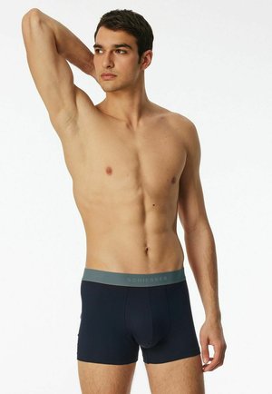 Navy blue boxer briefs feature a soft, elastic waistband with gray accents and a fitted shape. The material appears smooth and stretchy.