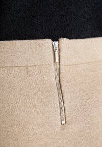 Tessuto in misto lana beige con un'apertura con zip visibile. La parte superiore è nera, creando un contrasto di colore tra i due materiali.