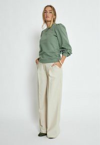 Green sweatshirt with puff sleeves, paired with cream wide-leg trousers. The outfit features a relaxed fit and is made from soft materials.
