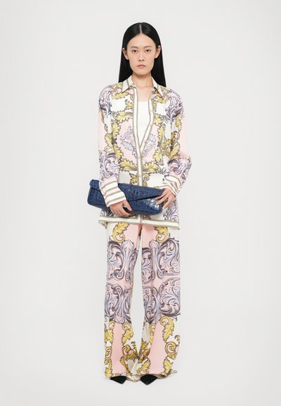 Costum din mătase imprimată, având modele florale intricate în nuanțe de roz, galben și gri. Modelul ține în mână o poșetă de mână bleumarin cu model de crocodil.