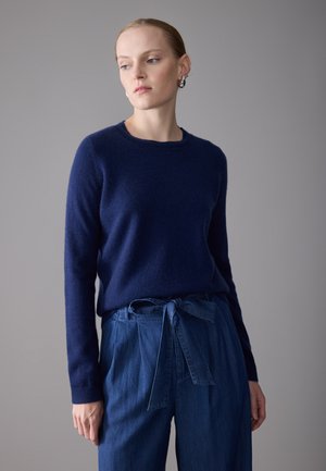 Mørkeblå strikkegenser med rund hals, strukturert stoff, kombinert med høyhullet denimbukser med en knyttet midjeaksent.