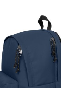 Mochila azul marino con una textura suave, que cuenta con dos tiradores de cremalleras, un asa en la parte superior y correas de hombro ajustables.