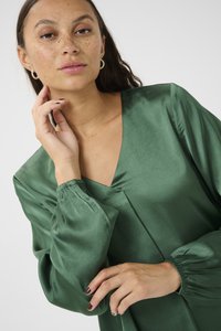 Grüne Satinbluse mit V-Ausschnitt und langen Puffärmel. Sie verfügt über eine glatte Textur und geraffte Manschetten, die ihr maßgeschneidertes Design unterstreichen.