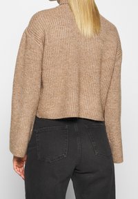 Chunky stickad kort tröja i ljusbrunt med hög halsringning och sänkta ax seams, kombinerad med svarta jeans med två bakfickor.