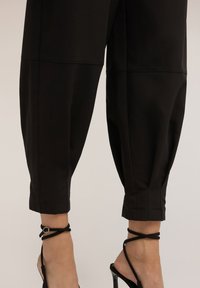 Pantalones negros recortados de tela lisa, con un corte ajustado, costuras visibles y una silueta relajada. Combinados con tacones negros de tiras.