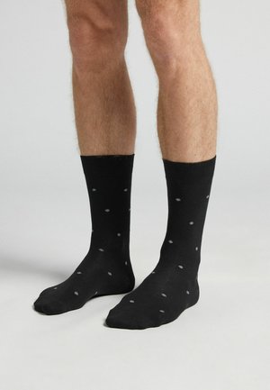 Chaussettes noires en tissu lisse, avec un motif de pois gris, dotées d'un bord côtelé et d'une longueur standard au-dessus de la cheville.