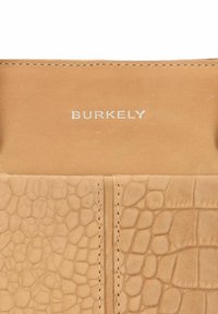 Portfel Burkely z brązowej skóry z tłoczonym wzorem krokodyla, gładką fakturą, białym logo i kontrastującymi detalami ściegów.