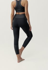 Czarny strój sportowy składający się z dopasowanego topu na krótki rękaw i legginsów wysokiego stanu. Legginsy mają gładką teksturę i kontrastowe boki.