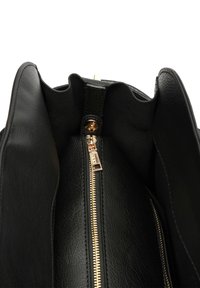 Unutrašnjost crne kožne torbe s glatkom teksturom, koja ima zlatni patentni zatvarač i dugme za zatvaranje. Mekani rubovi i strukturiran oblik.