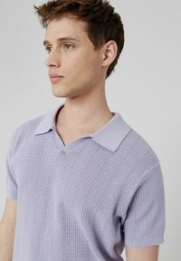 Polo en tricot violet clair avec un col en V et des manches courtes, présentant un motif texturé et un col doux.