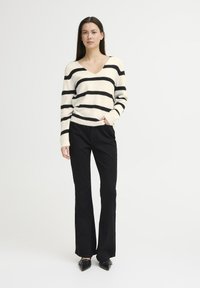 Striped cream and black sweater with a V-neck and ribbed cuffs, paired with black flared pants and pointed-toe black shoes.