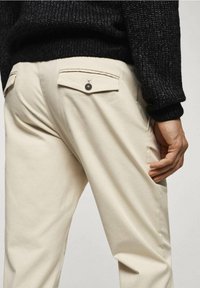 Beige Baumwollhosen mit Gesäßtaschen mit Klappen und Knopfverschluss, kombiniert mit einem strukturierten schwarzen Strickpullover.