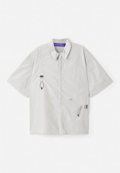 Srajca s kratkimi rokavi in ovratnikom v svetlo sivi barvi, z vrvicami na straneh in natisnjenim logotipom na zgornjem delu prsi. Gladka, lahka tkanina.