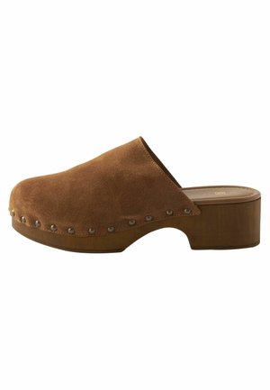 Sabot en suede marron avec un bout arrondi, un talon en bois et des clous décoratifs le long du bord. Texture lisse avec un design décontracté.