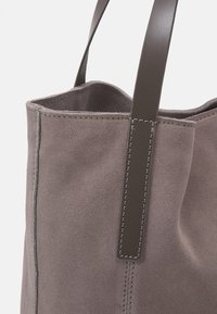 Grau Wildleder-Shopper mit dunklen Ledergriffen und sichtbaren Nähten. Offene Oberseite mit weicher Textur und strukturierten Seiten.