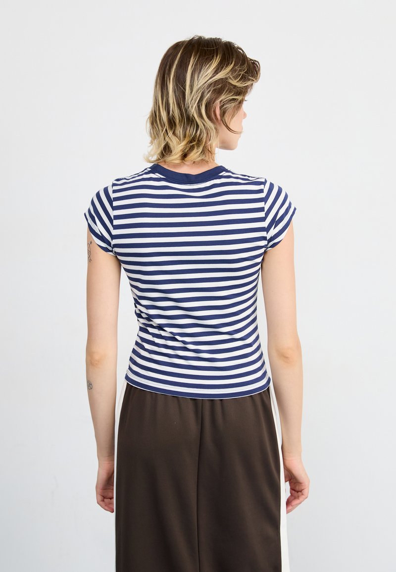 T-shirt a righe con strisce orizzontali blu navy e bianche, maniche corte e colletto a girocollo, abbinato a pantaloni larghi marroni.