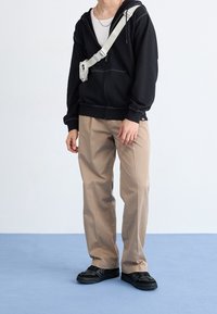 Černá mikina na zip, béžové kalhoty rovného střihu, černé texturované tenisky, kabelka přes tělo v světle šedé barvě. Jednoduchý design s minimálními akcenty.