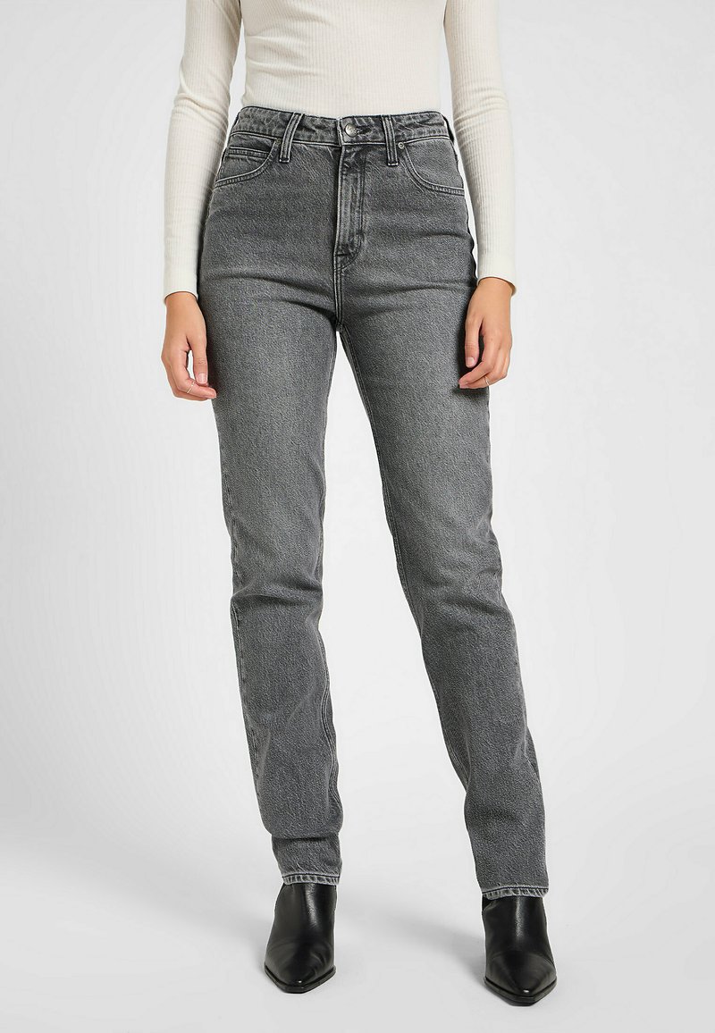 Vaqueros negros de cintura alta en un lavado desvanecido, diseño de pierna recta, con cinco bolsillos y costuras visibles. Llevados con una blusa ajustada y botas.