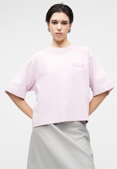 Ροζ βαμβακερό t-shirt με χαλαρή, κουβερτούρα εφαρμογή, κοντά μανίκια και ανάγλυφο κείμενο στο στήθος. Φορέθηκε με γκρι φούστα.