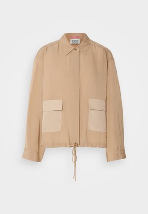 Veste légère beige à manches longues, col, ourlet à cordon et deux poches plaquées à l'avant dans une teinte légèrement plus foncée. Texture lisse.