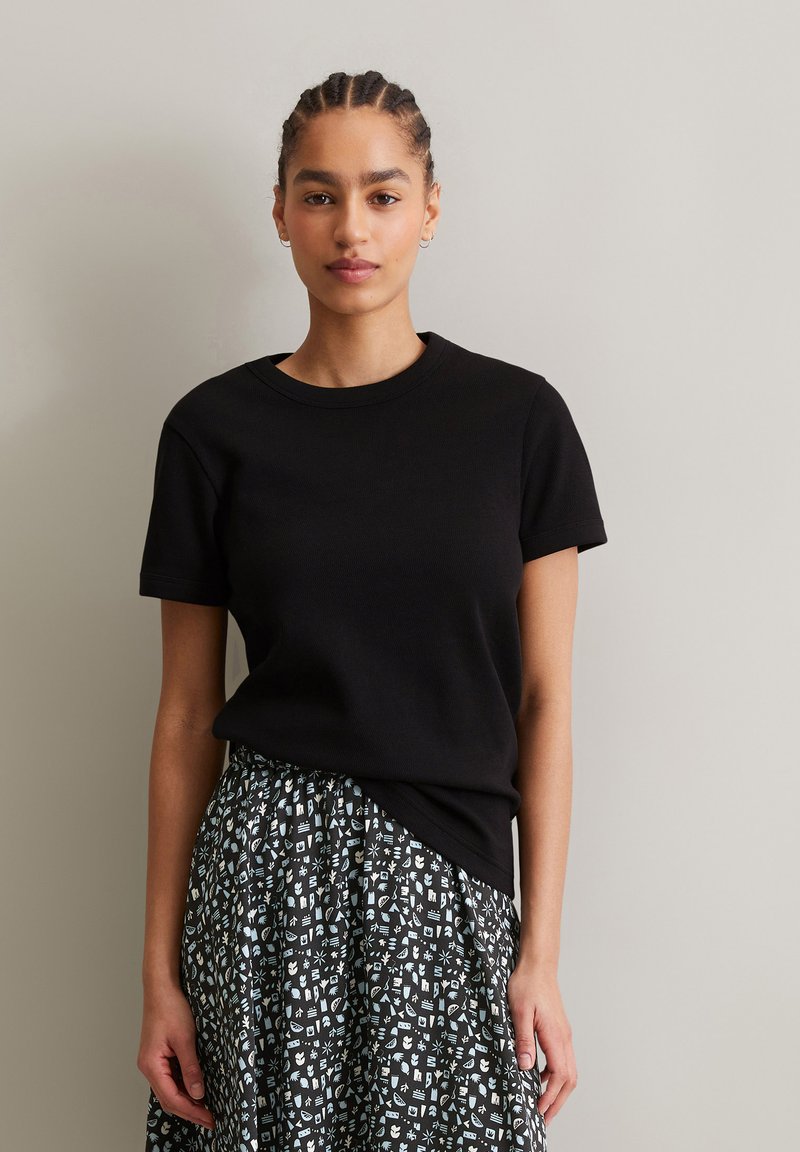 Schwarzes kurzärmliges T-Shirt aus Rippstruktur, kombiniert mit einem gemusterten Rock mit schwarzem Hintergrund und aufwendigen hellblauen Motiven.